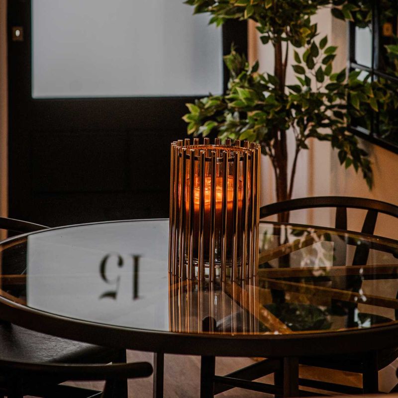 A gold cylindrical candle holder on a round glass dining table with dark chairs - a styling detail from the Coastal Residence by Atlantic Interiors