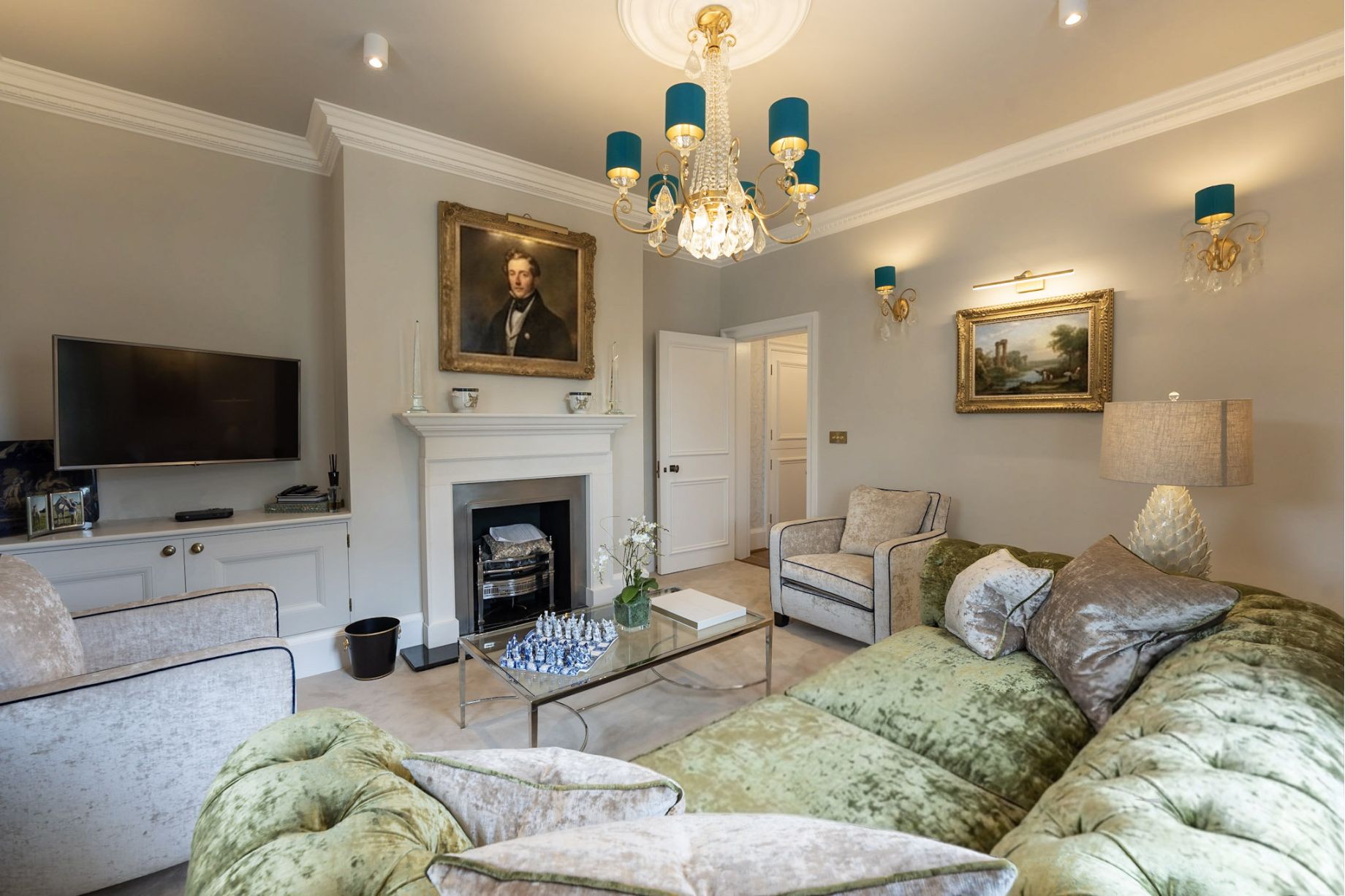 A luxury living room with green velvet tufted sofas, a teal and crystal chandelier, white fireplace and portrait painting - residential interior design by Atlantic Interiors