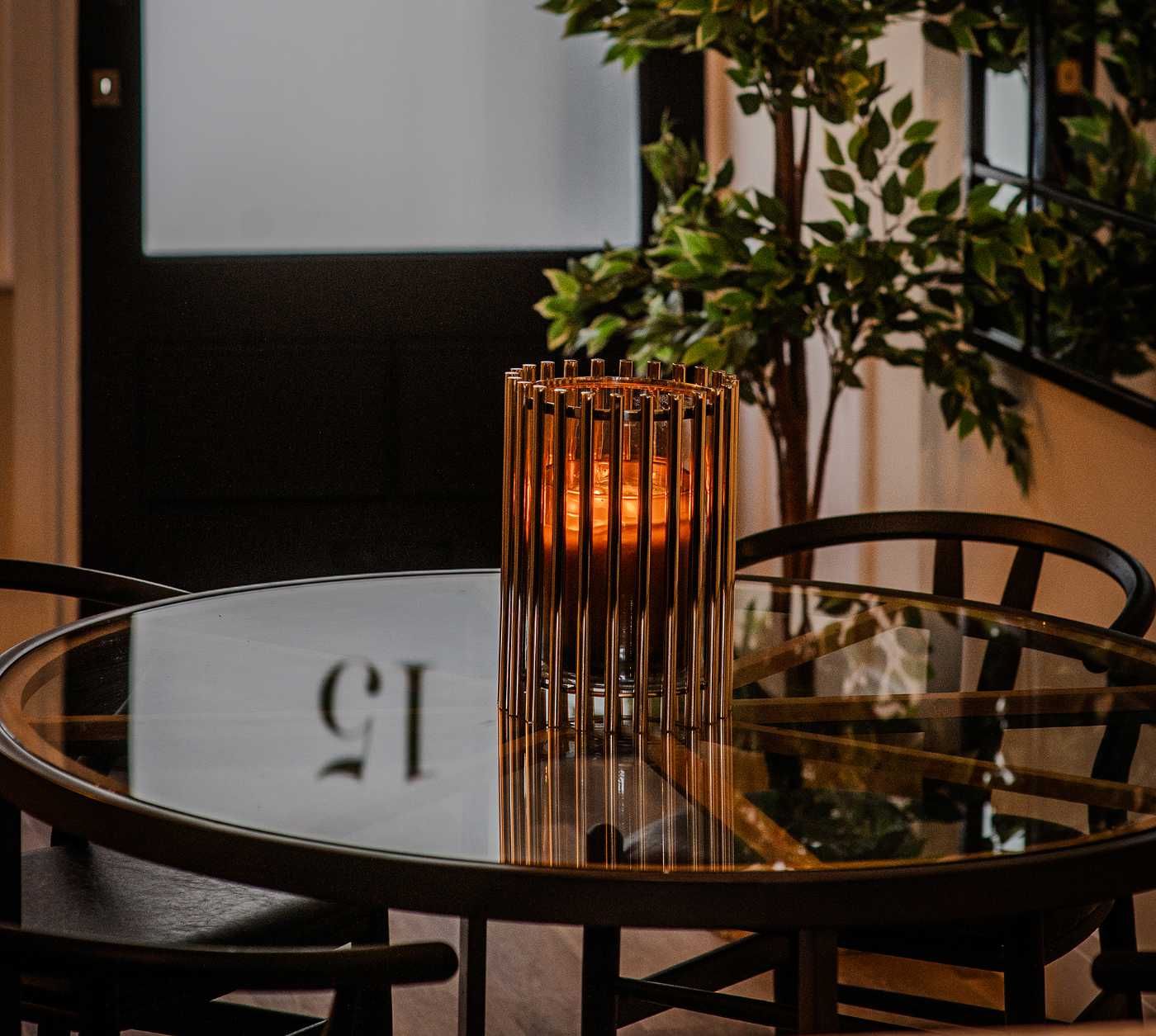 A gold cylindrical candle holder on a round glass dining table with dark chairs - a styling detail from the Coastal Residence by Atlantic Interiors