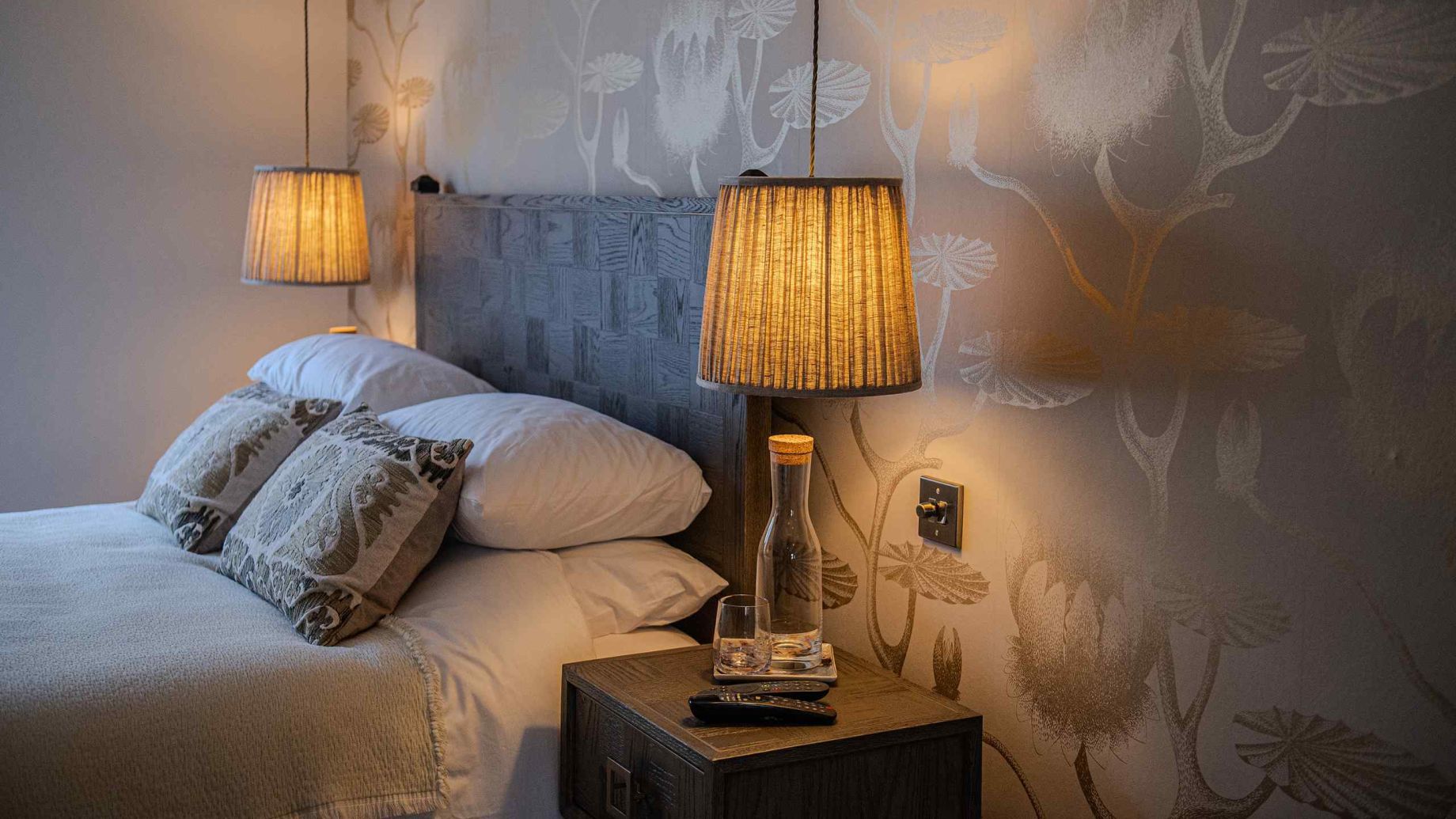 A luxury bedroom with botanical wallpaper, a dark wood headboard, and warm pendant lamps - residential interior design by Atlantic Interiors