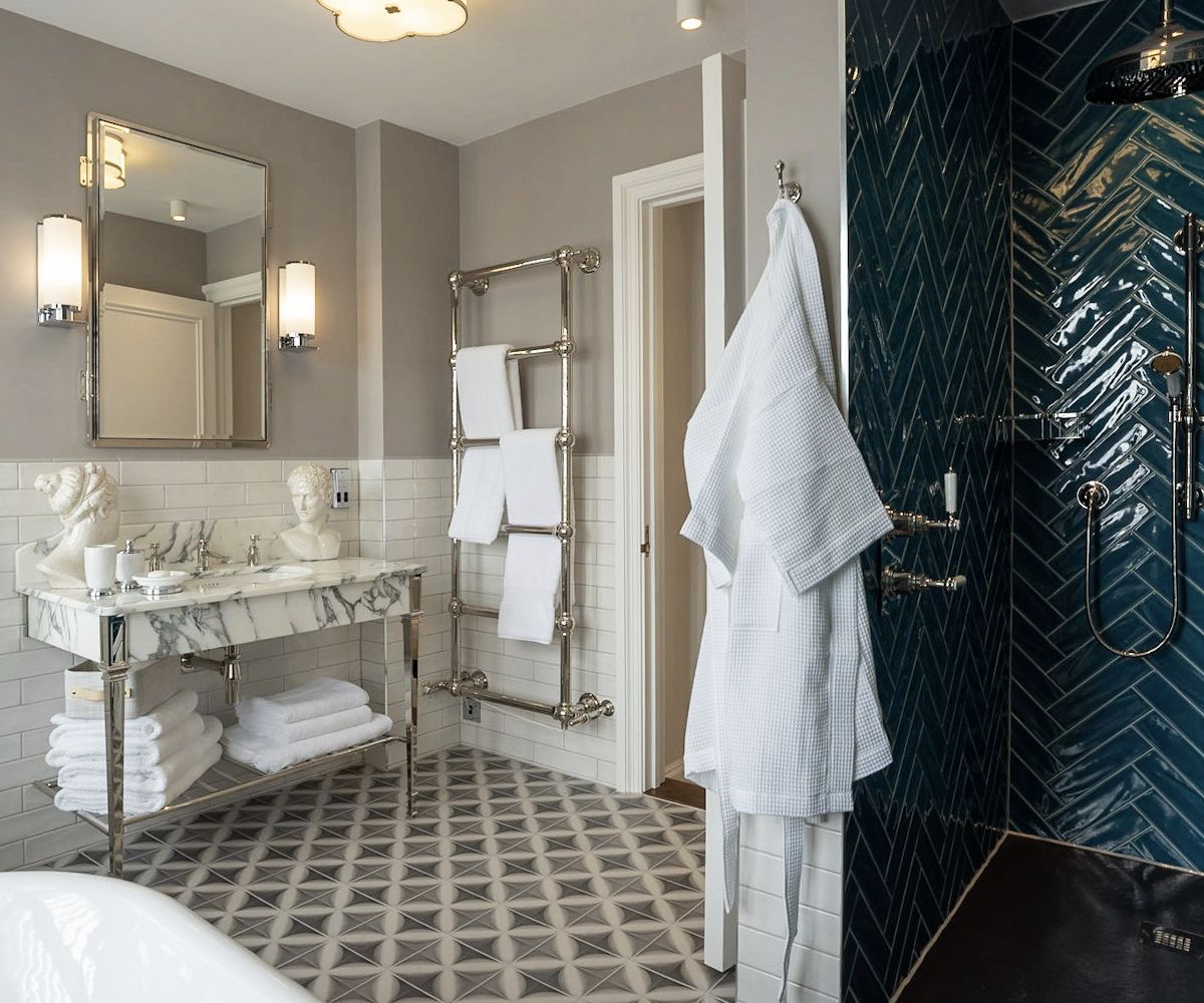 A classic luxury bathroom with a marble washstand, chrome heated towel rail, wall sconces and geometric patterned floor tiles - interior design by Atlantic Interiors
