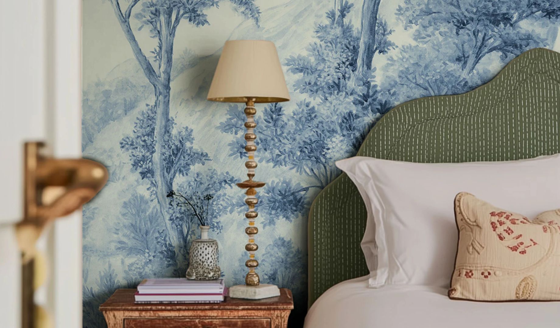 A luxury bedroom with a blue toile landscape wallpaper mural, a curved green upholstered headboard and a gold table lamp - interior design by Atlantic Interiors