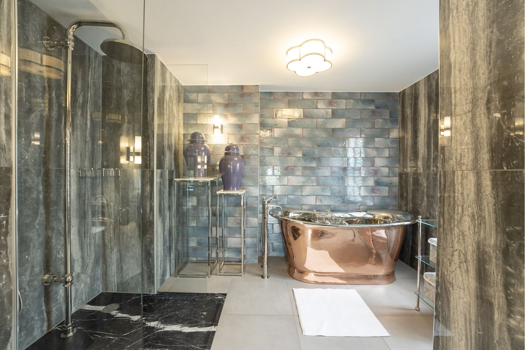 A luxury bathroom with a polished copper freestanding bath, iridescent blue-green glazed brick tiles, glass shower enclosure and chrome rainfall showerhead - residential interior design by Atlantic Interiors